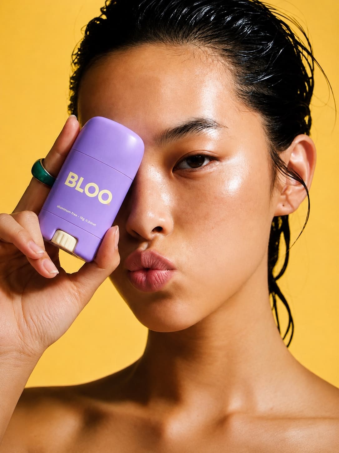 Concept publicitaire : portrait beauté, stick déodorant BLOO violet tenu devant l'œil sur fond jaune.